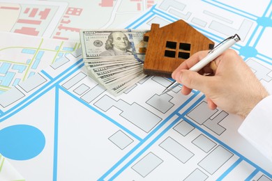 Cartographer with house model and money drawing cadastral map, closeup