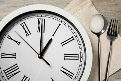Photo of Wall clock and cutlery on light wooden table, closeup. Business lunch concept