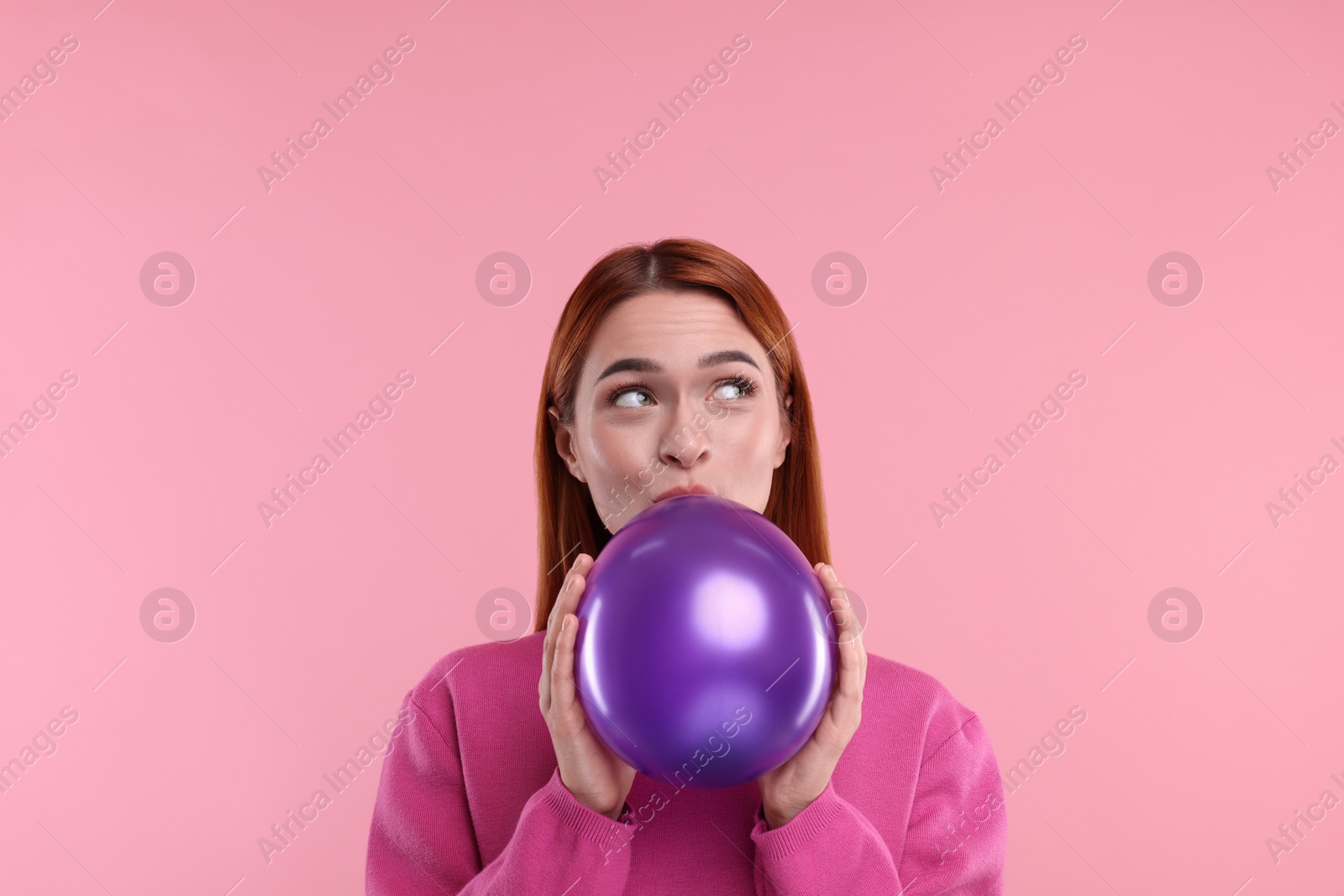 Photo of Woman inflating purple balloon on pink background