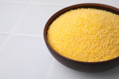 Raw cornmeal in bowl on white tiled table, closeup. Space for text