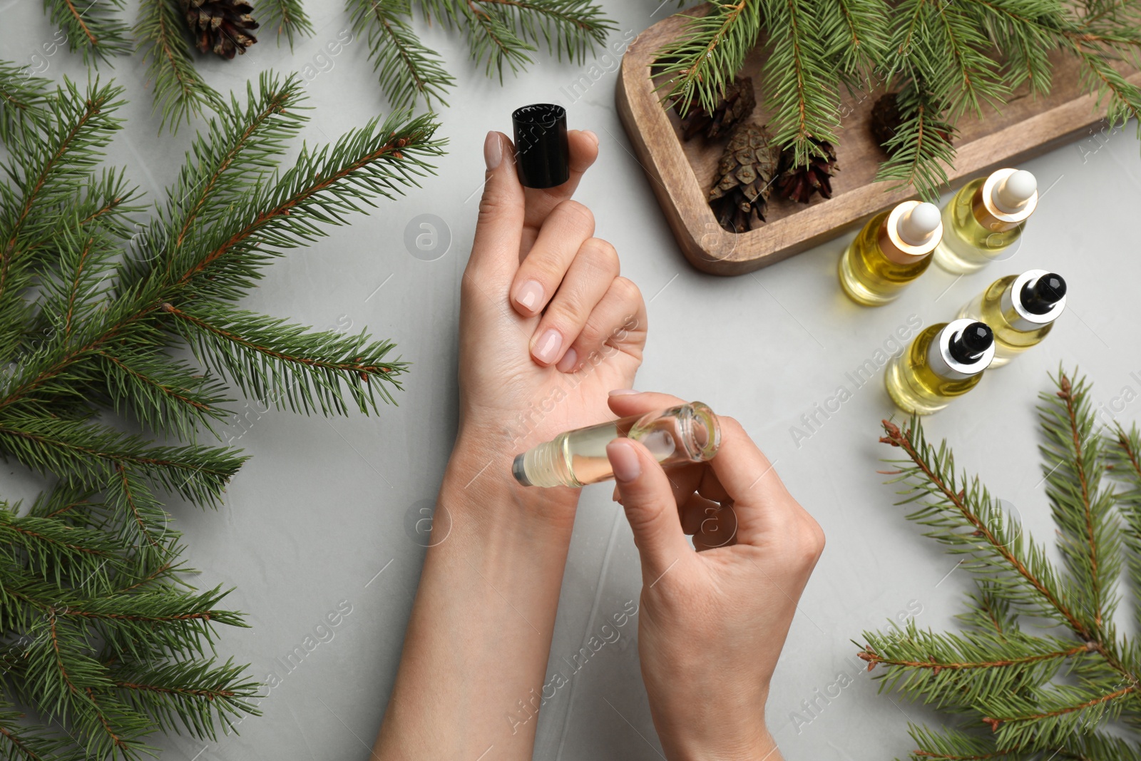 Photo of Woman applying pine essential oil on wrist at grey table, top view