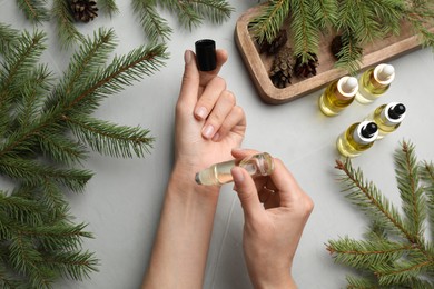 Photo of Woman applying pine essential oil on wrist at grey table, top view