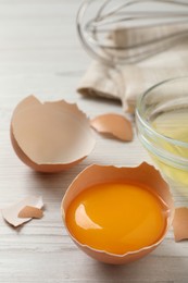 Photo of Raw yolk in broken chicken eggshell on wooden table, closeup