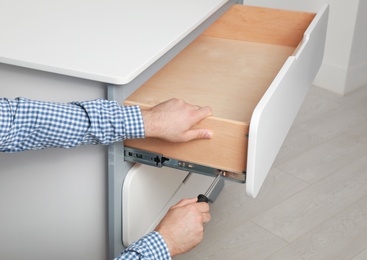 Man repairing chest of drawers in room, closeup