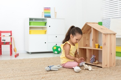 Photo of Cute little playing with toys near wooden house on floor at home, space for text