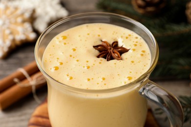 Photo of Glass of delicious eggnog with anise star on table, closeup
