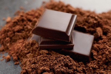 Photo of Delicious dark chocolate and cocoa powder on table, closeup