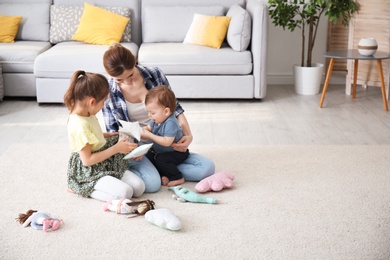 Photo of Mother with cute little children sitting on cozy carpet at home