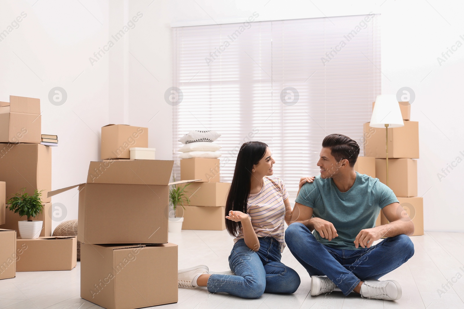 Photo of Happy couple in room with cardboard boxes on moving day