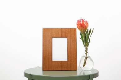 Photo of Blank frame and vase with flower on table against white background. Mock up for design