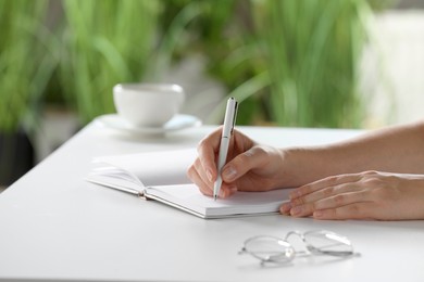 Photo of Woman writing in notebook at white table indoors, closeup