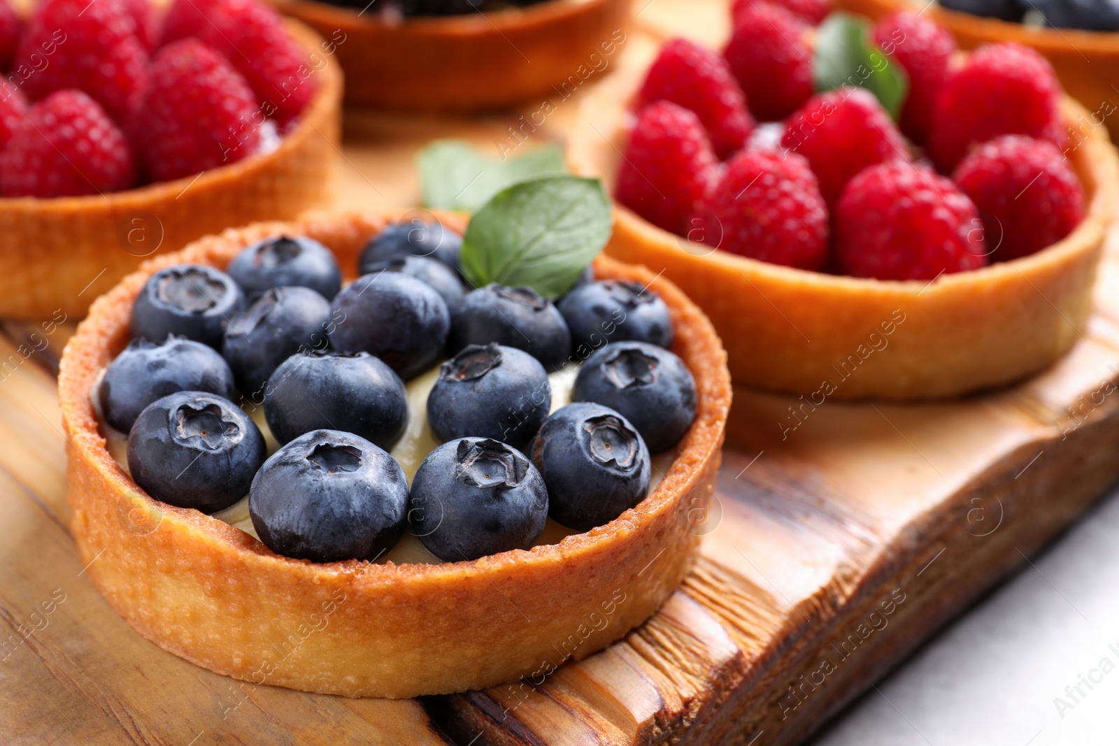 Photo of Tartlet with fresh blueberries on wooden board, closeup. Delicious dessert