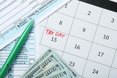 Photo of Tax day. Calendar with date reminder, documents, pen and dollar banknotes on table, flat lay