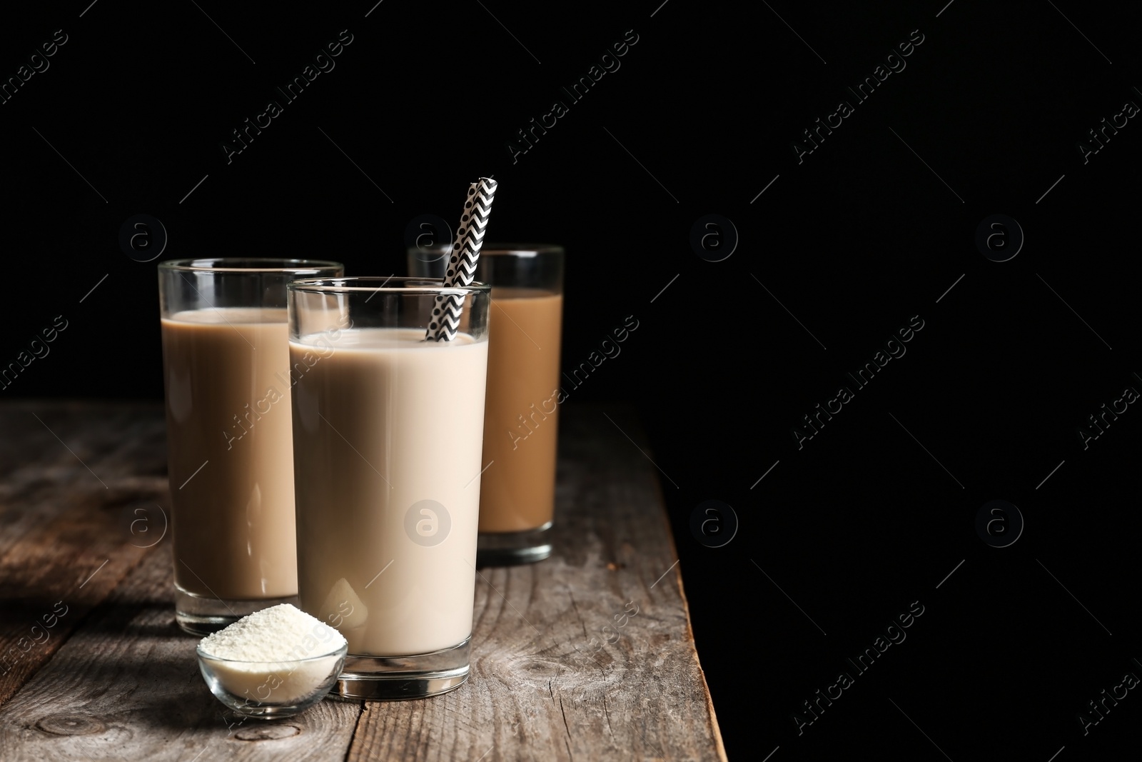 Photo of Glasses with protein shakes and powder in bowl on table against black background. Space for text