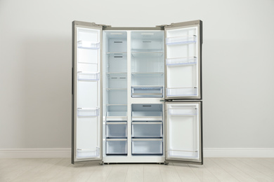 Photo of Modern empty refrigerator near light grey wall. Home appliance