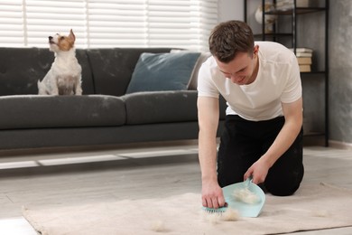 Smiling man with brush and pan removing pet hair from carpet at home. Space for text