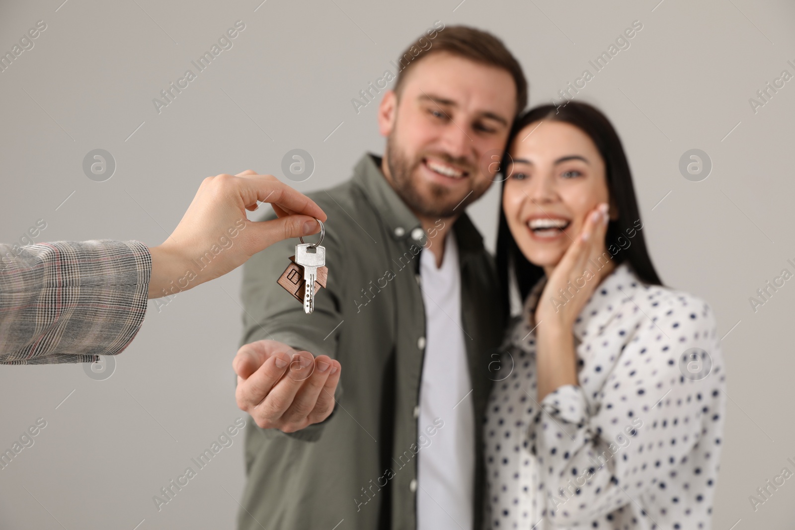 Photo of Real estate agent giving key to happy young couple against grey background, focus on hands