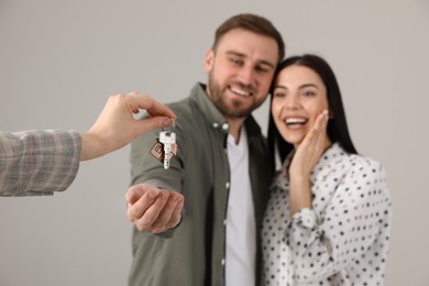 Photo of Real estate agent giving key to happy young couple against grey background, focus on hands