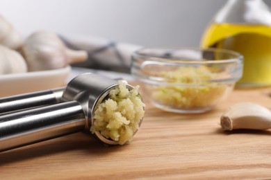 Photo of One metal press and garlic on wooden table, closeup