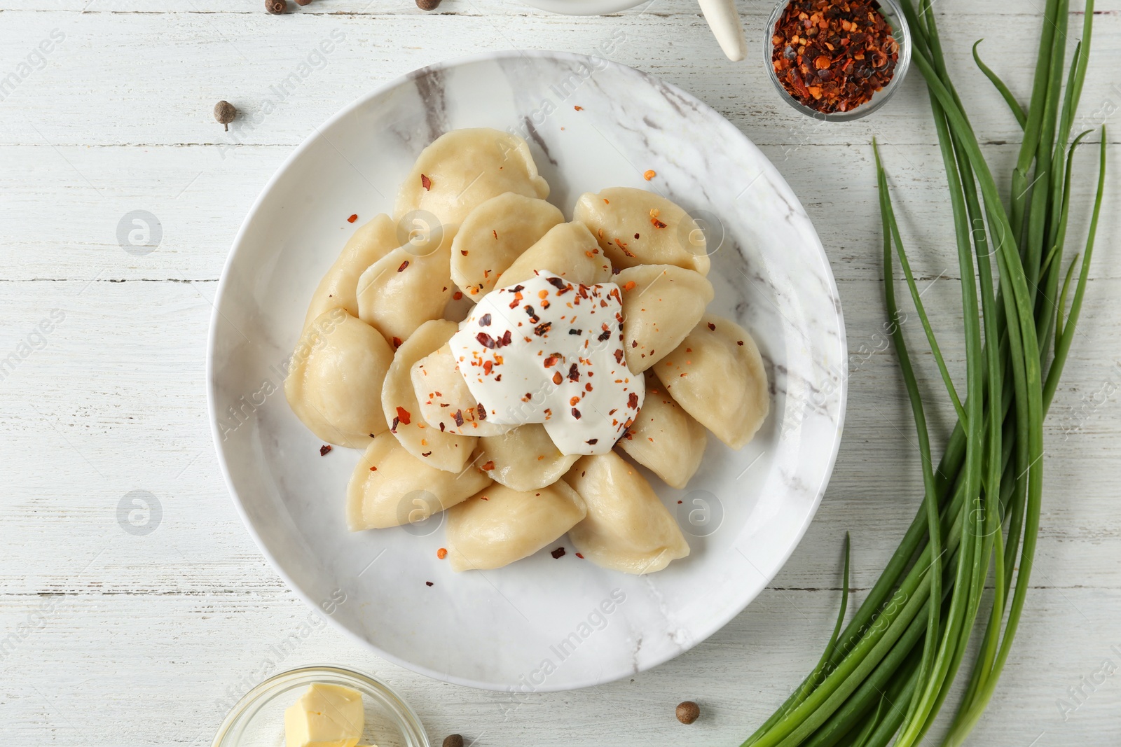 Photo of Delicious cooked dumplings with sour cream on white wooden table, flat lay