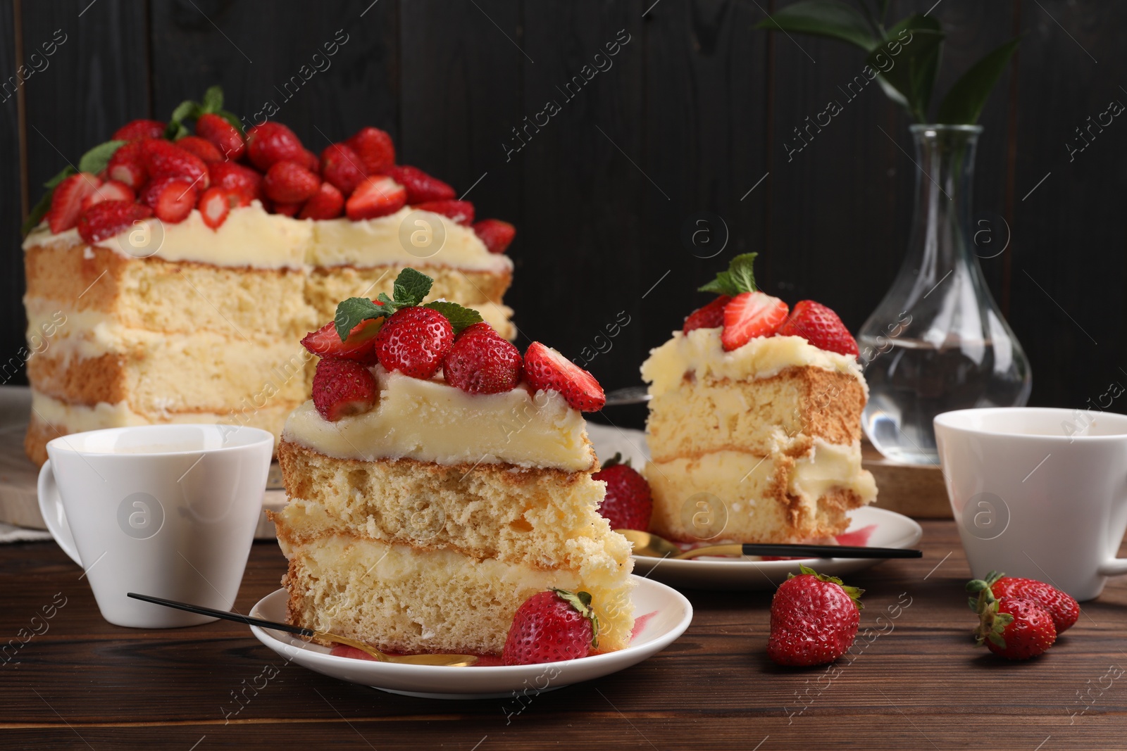 Photo of Tasty cake with fresh strawberries, mint and cups of drink on wooden table