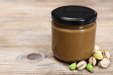 Tasty nut paste in jar and pistachios on wooden table, closeup. Space for text