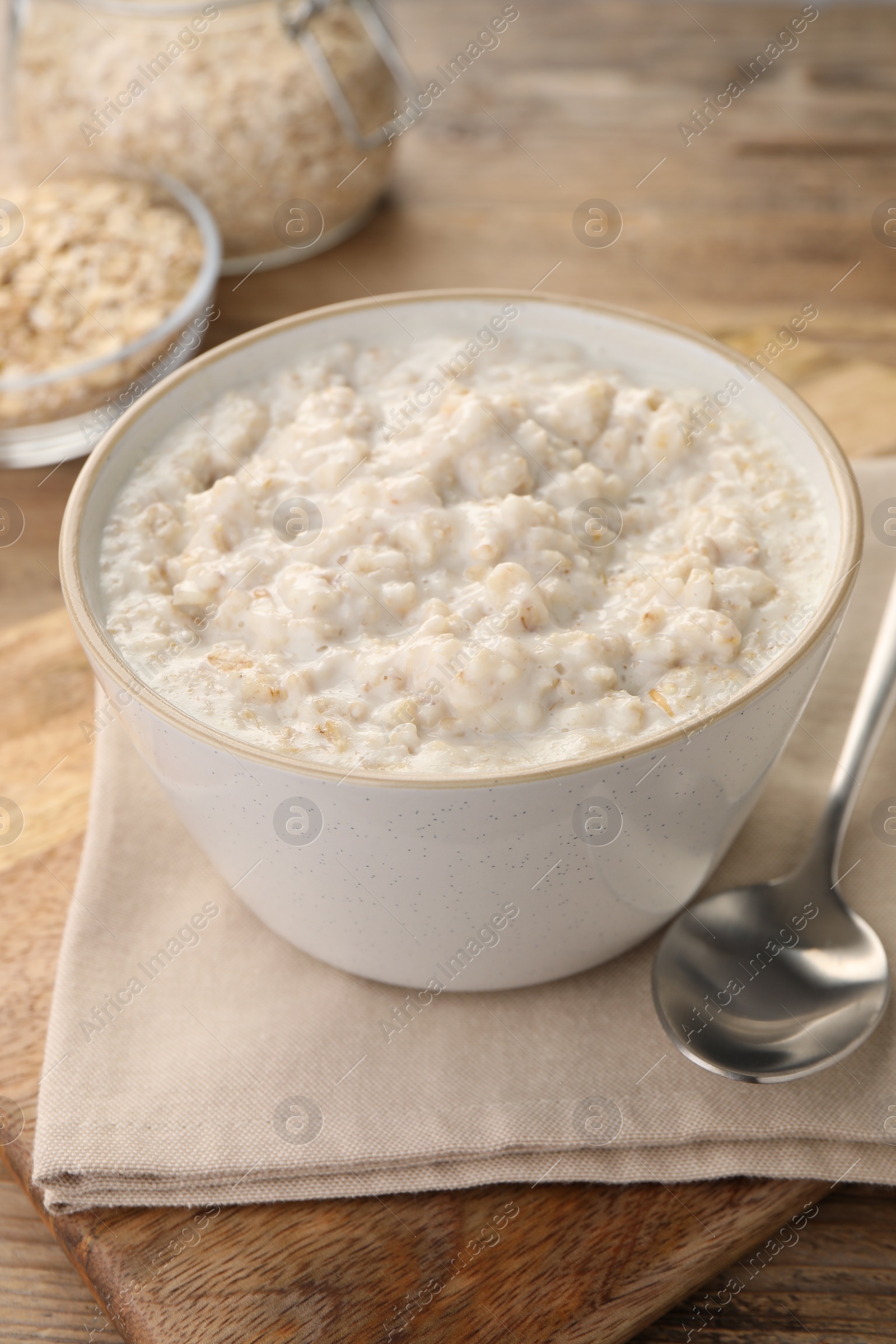 Photo of Tasty boiled oatmeal in bowl and spoon on wooden table