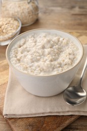 Photo of Tasty boiled oatmeal in bowl and spoon on wooden table