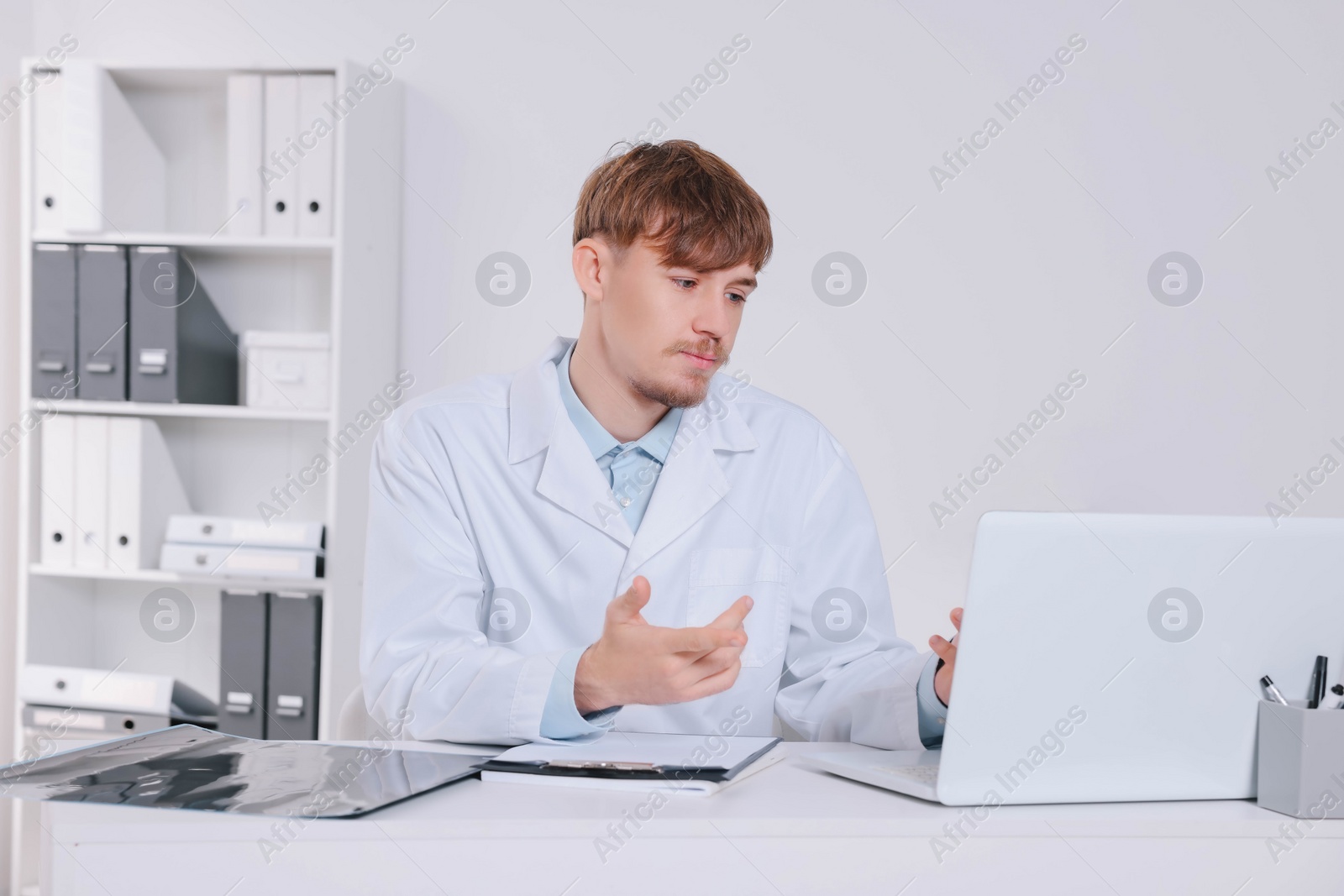 Photo of Doctor consulting patient on laptop at table in clinic. Neck MRI