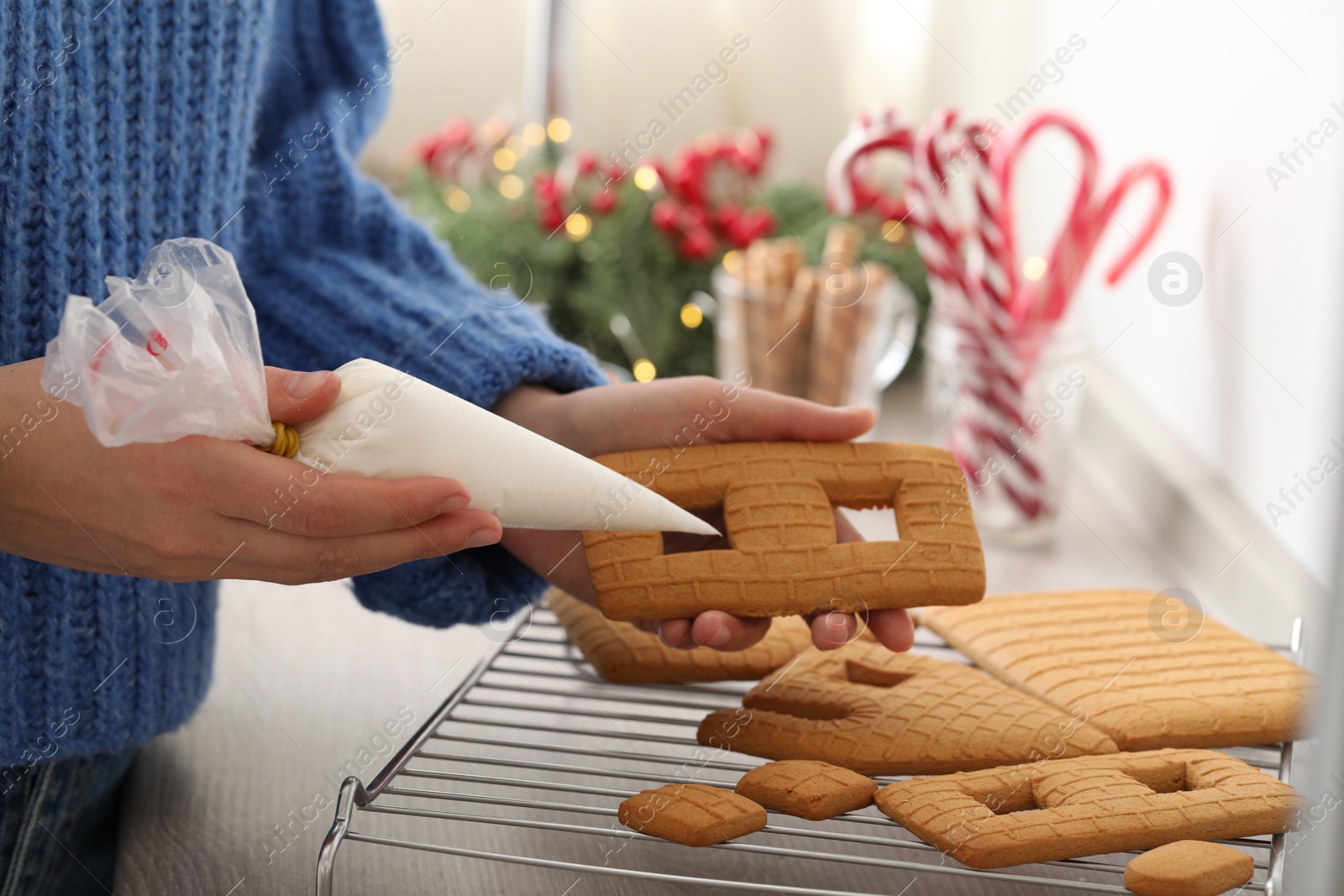 Photo of Woman making gingerbread house at wooden table, closeup