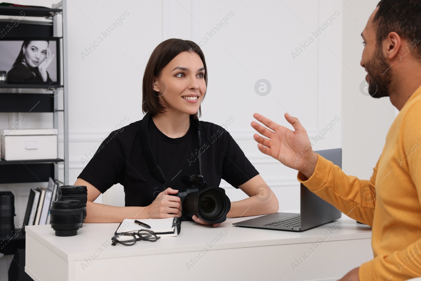 Photo of Young professional photographer holding camera while talking with man in modern photo studio