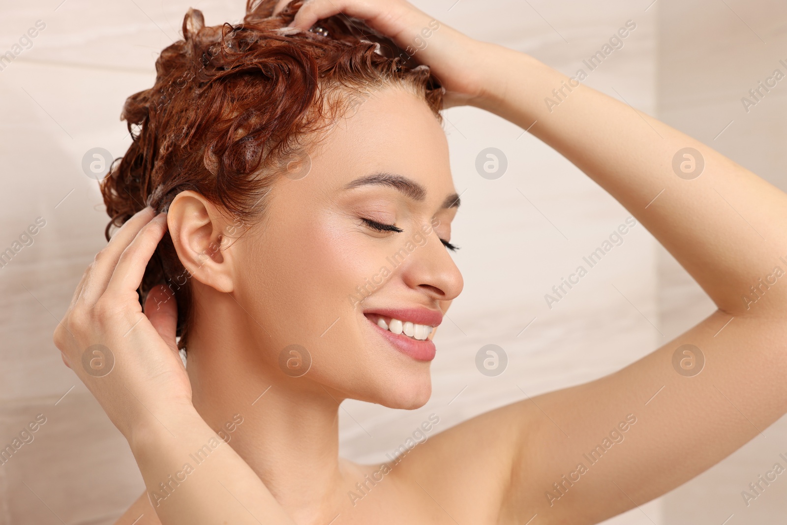 Photo of Happy young woman washing her hair with shampoo in shower