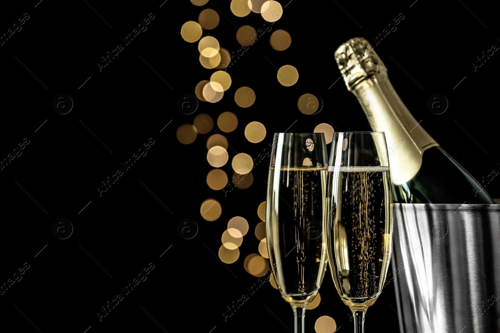 Photo of Glasses of champagne near bucket with bottle against blurred lights, space for text