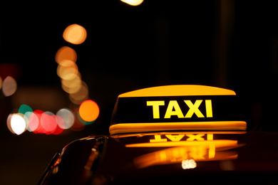 Taxi car with yellow roof sign on city street at night, closeup