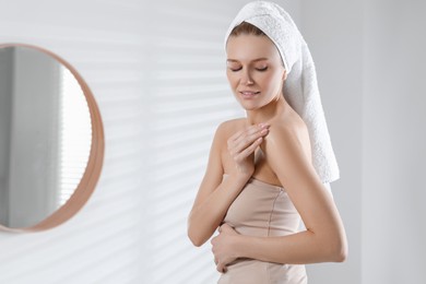 Photo of Beautiful woman applying body oil onto shoulder in bathroom, space for text