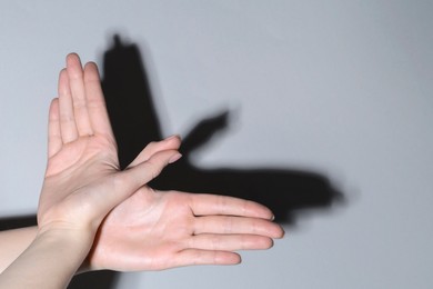 Shadow puppet. Woman making hand gesture like bird on light background, closeup