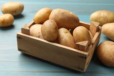 Photo of Raw fresh potatoes in crate on light blue wooden table