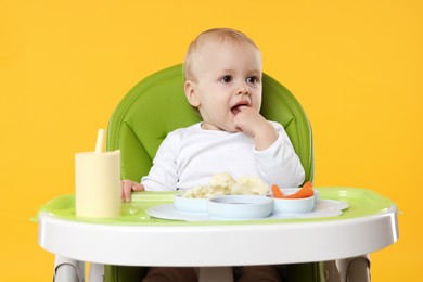Photo of Cute little baby with healthy food in high chair on orange background