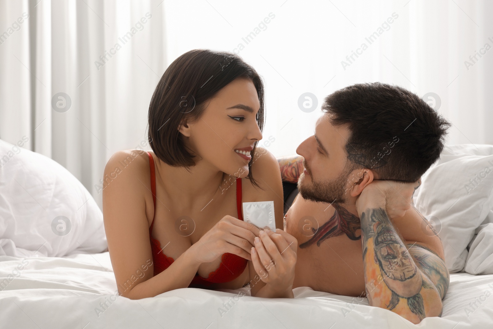 Photo of Young couple holding condom in bedroom. Safe sex