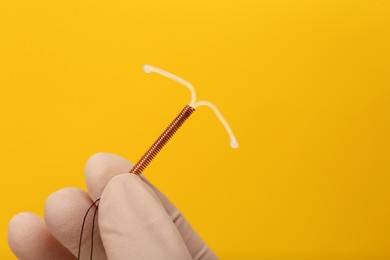 Photo of Doctor holding T-shaped intrauterine birth control device on yellow background, closeup