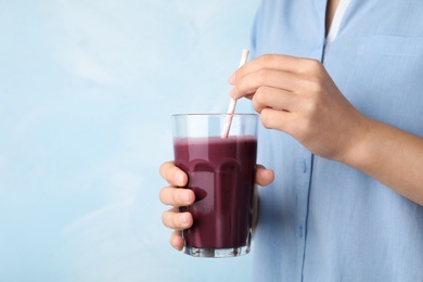 Photo of Woman with glass of fresh acai drink and straw on light blue background, closeup. Space for text