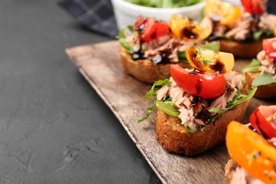 Photo of Delicious bruschettas with balsamic vinegar, tomatoes, arugula and tuna on grey textured table, closeup. Space for text