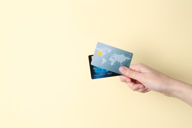 Woman holding credit cards on pale yellow background, closeup. Space for text