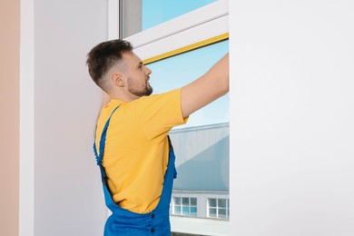 Photo of Worker in uniform measuring window with tape indoors. Roller blinds installation