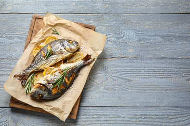 Photo of Delicious roasted fish with lemon on grey wooden table, flat lay. Space for text