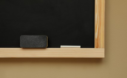 Photo of Clean blackboard with chalk and duster hanging on beige wall