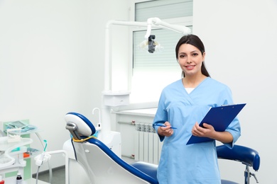 Photo of Portrait of professional female dentist with clipboard in clinic. Space for text