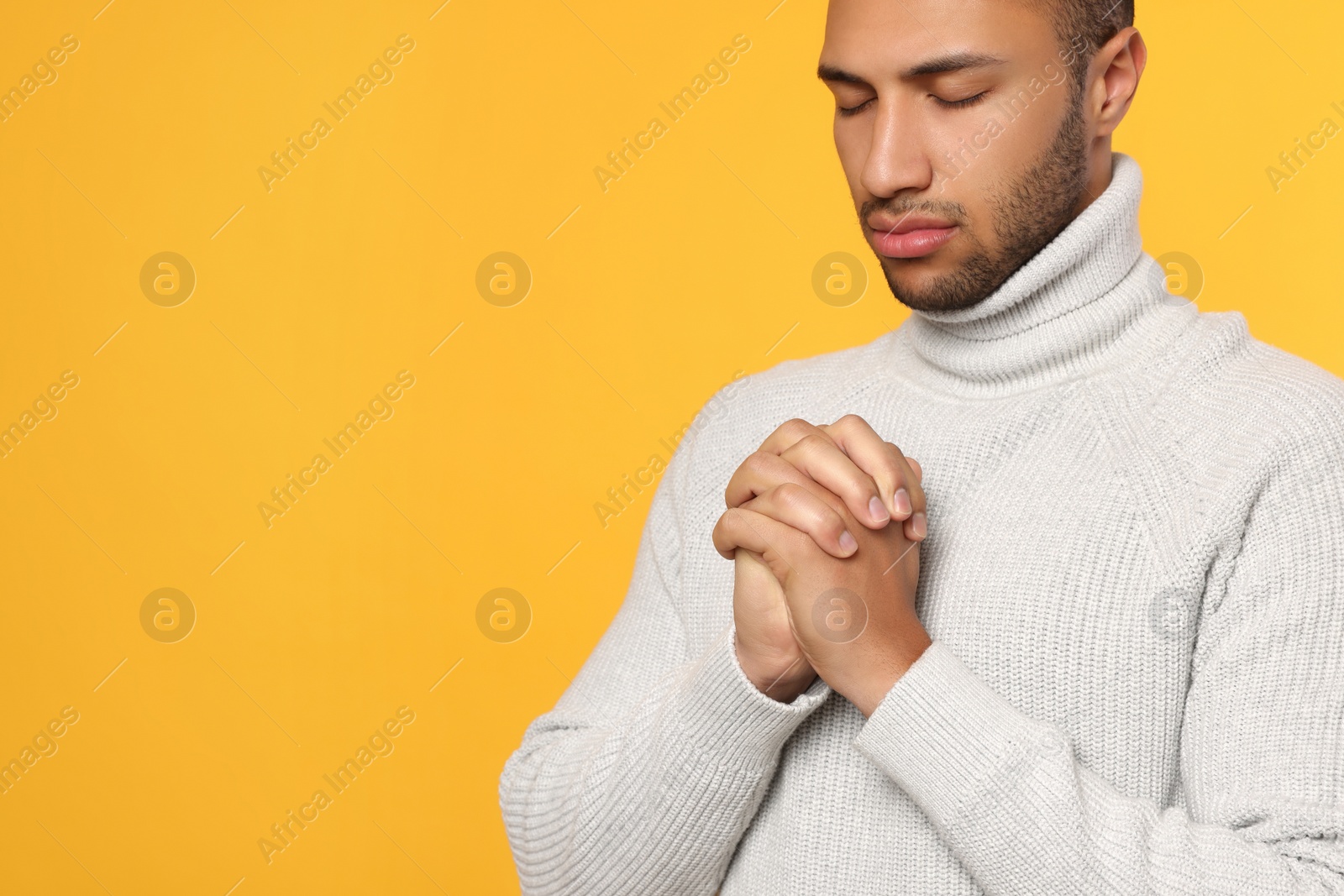 Photo of African American man with clasped hands praying to God on orange background. Space for text
