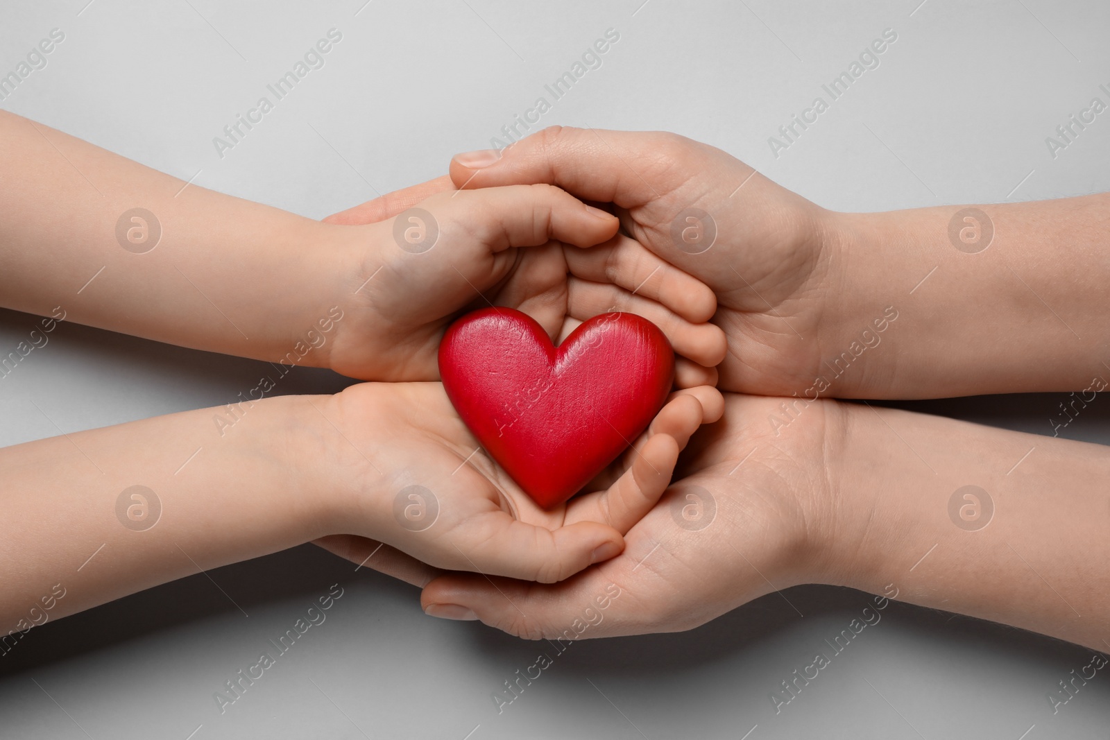 Photo of Woman and kid holding red heart in hands on light grey background, top view
