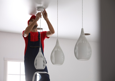 Photo of Worker installing lamp on stretch ceiling indoors
